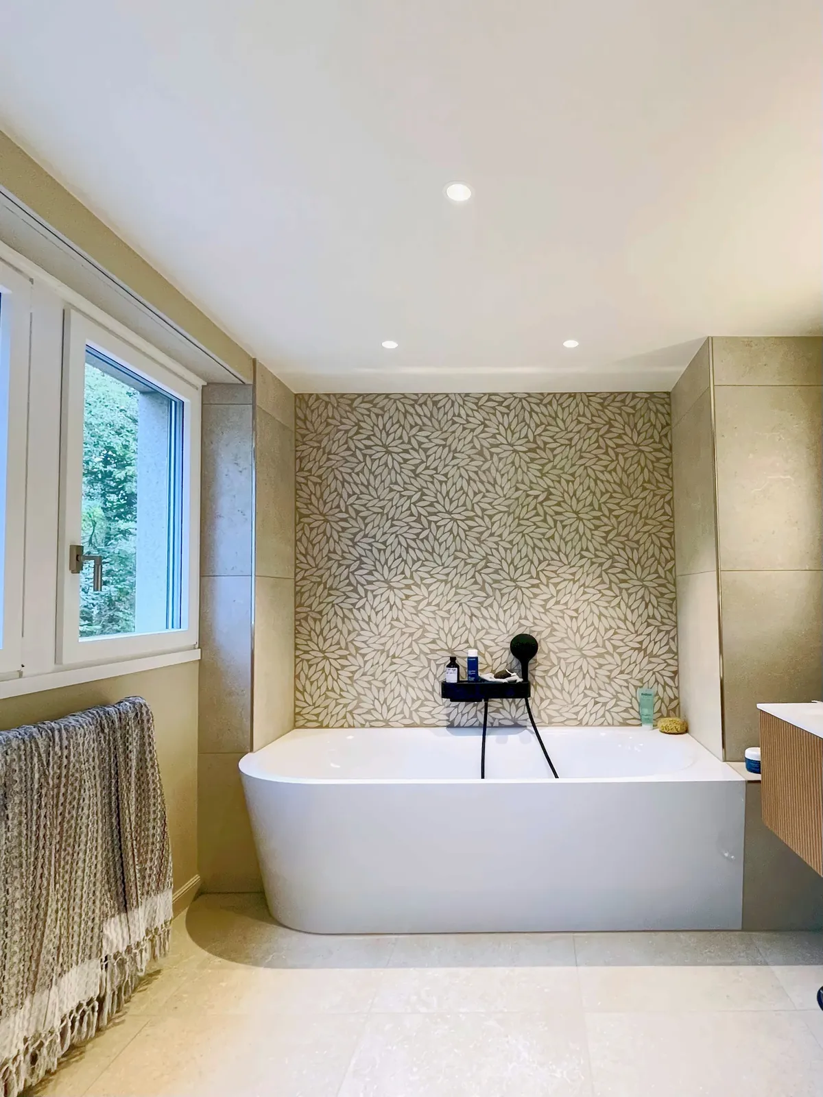 Zwei Räume, komplett neu gestaltet: ein Bad mit Wanne vor einer Wand aus Blättermosaik, ein Duschraum mit türkisem Mosaik und bodenebener Dusche.